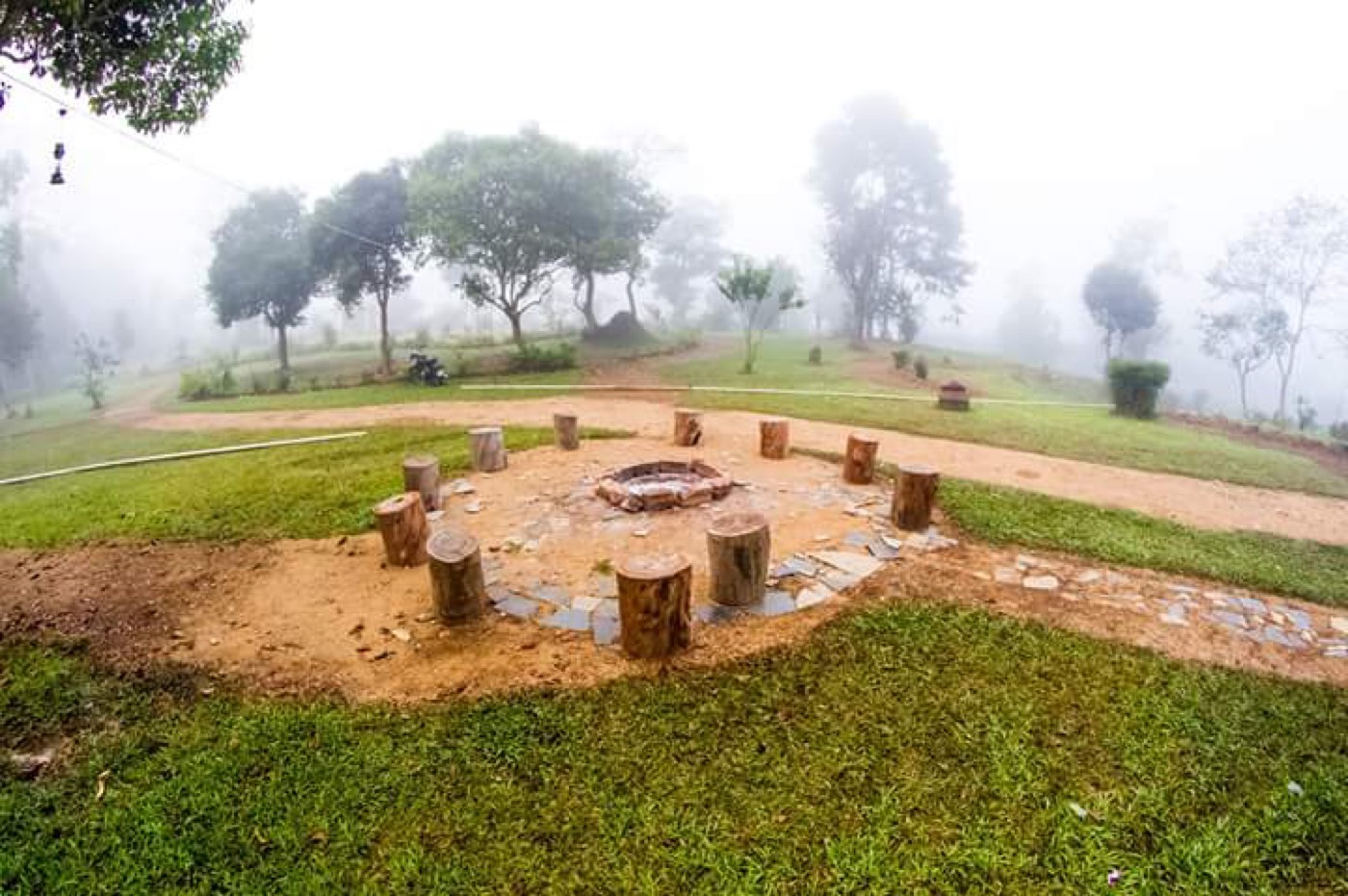 Stone fire pit with log seats on a misty lawn