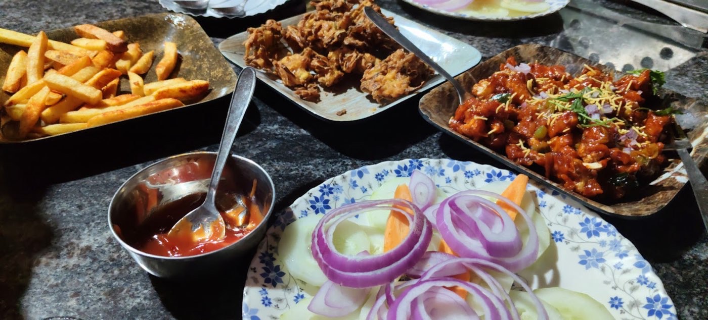 Plates of fried snacks, curry and fresh onion salad